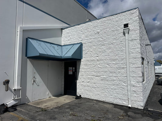 The glass front door of Tour Essentials, below a blue metal awning on a grey brick building.