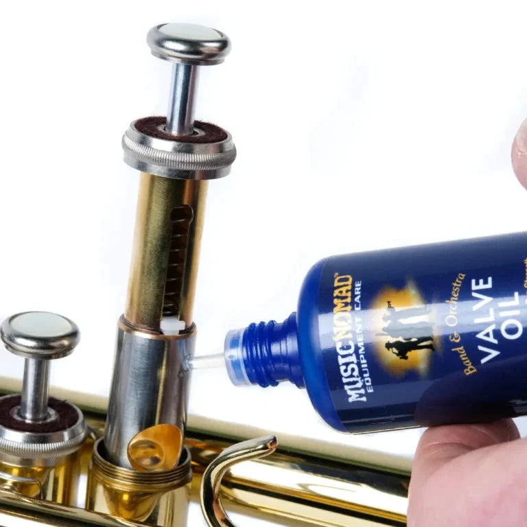 Music Nomad Valve Oil Pure Synthetic bottle beside brass instrument valve assembly, blue bottle